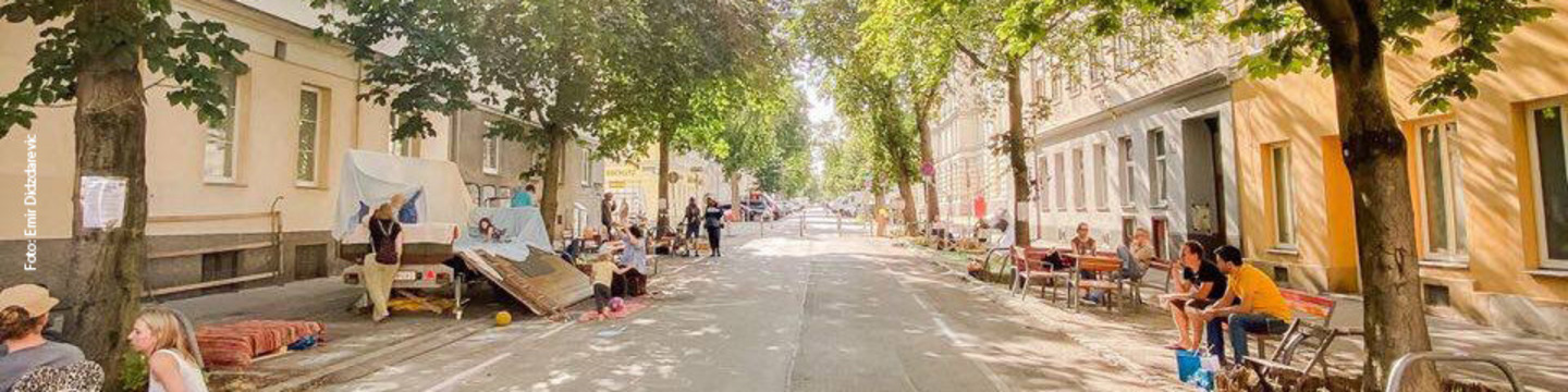 Sommeroase Hasnerstaße an einem sonnigen Tag mit Menschen die freie Parkplätze nutzen.
